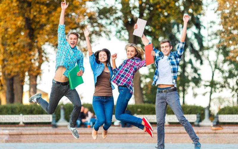 Funny young students are jumping together in park.