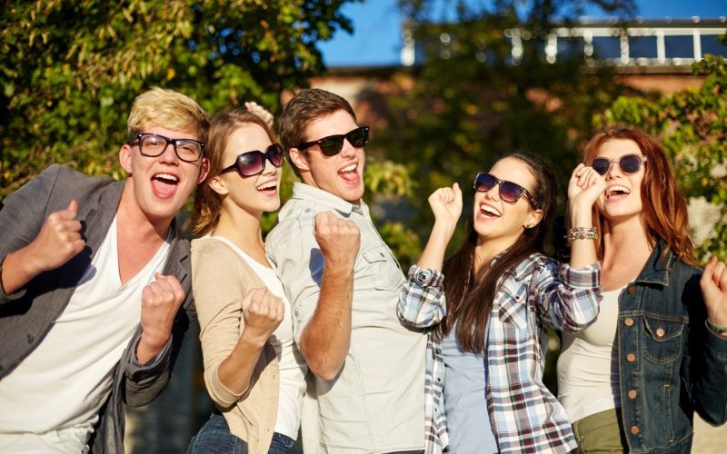 summer holidays, friendship, achievement and success concept - group of happy friends showing triumph gesture at campus or city park